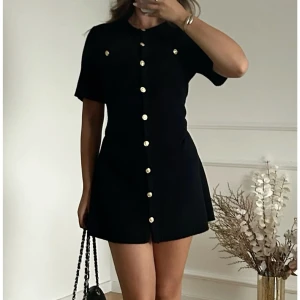Svart kortklänning med knappar  - Snygg elegant svart kortklänning med guldknappar framtill från H&M. Klänningen har korta ärmar och en figurnära passform. Perfekt för en stilren look. Säljer denna klänning då jag upplever att den är för stor för mig har använt en gång. Storlek S. 