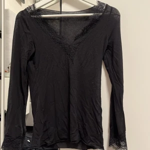 Svart långärmad topp med spetsdetaljer från inimisimi  - Snygg svart långärmad topp med v-ringning och spetsdetaljer vid hals och ärmslut. Perfekt för en stilren look. Från intimissimi 