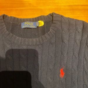 Mörkblå kabelstickad tröja från Ralph Lauren - Säljer en stilren mörkblå kabelstickad tröja från Ralph Lauren med det klassiska röda logotypbroderiet på bröstet. Tröjan är endast använd ett fåtal gånger och är som ny!