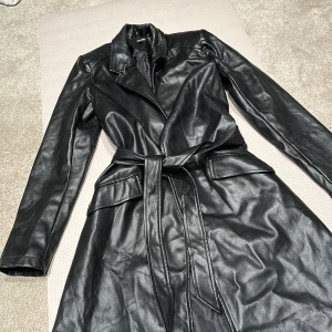 Svart trenchcoat från Bubbleroom - Snygg svart trenchcoat från Bubbleroom by Molly Rustas. Jackan har ett bälte i midjan och långa ärmar. Perfekt för en stilren look.