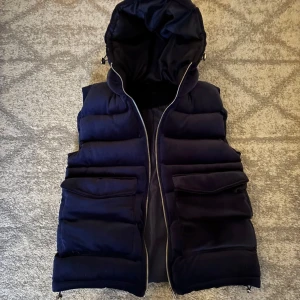 Vendiera väst  - Säljer denna snygga mörkblåa dunvästen från vendiera med dragkedja och praktiska fickor. Västen är perfekt för kyligare dagar. Den quiltade designen ger en modern look. Västen är i nyskick då den aldrig är använd 