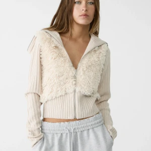 Beige ribbad jacka med fuskpälsdetaljer - Snygg beige jacka med ribbad design och fuskpälsdetaljer framtill. Jackan har en dragkedja och långa ärmar, perfekt för kyligare dagar. Den croppade stilen ger en modern look. Ny med prislapp på och nypris är 499kr