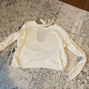 Vit ribbad tröja med knytband - Säljer en stilren vit ribbad tröja med långa ärmar och ett knytband i nacken. Tröjan har en öppen rygg som ger en elegant touch. Perfekt för att lägga till en chic detalj i din garderob.