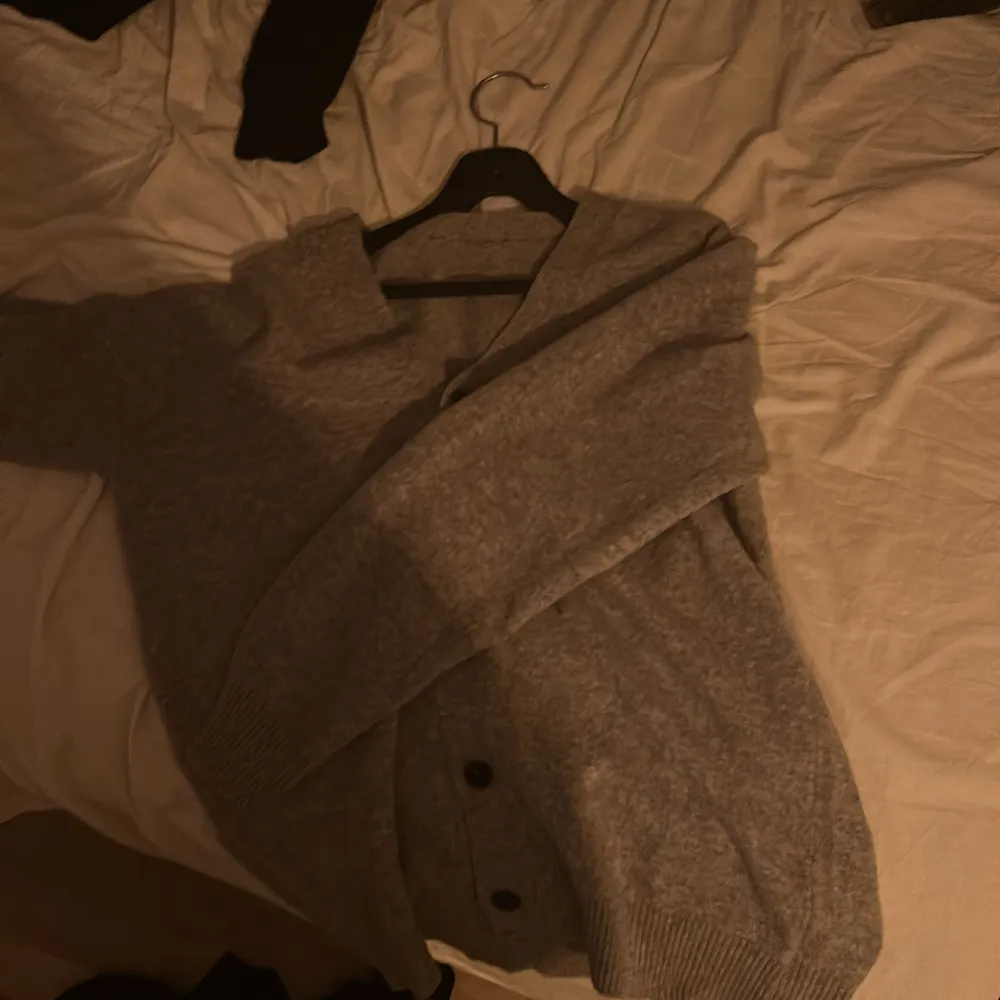 Säljer en mysig grå kofta med knappar framtill. Perfekt för kyliga dagar och enkel att matcha med olika outfits. Den har långa ärmar och ribbade muddar vid ärmslut och nederkant.. Neuletakit & Villapaidat.