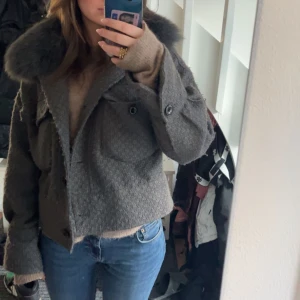 Grå kappa med pälsdetalj från Meotine - Säljer en superfin grå kappa från Meotine i storlek S/M. Den har en stor, fluffig pälsdetalj vid kragen och knappar framtill. Perfekt för höst och vinter, och ger en lyxig känsla. Passar både till vardags och festliga tillfällen.