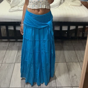 Blå långkjol med volangdetaljer - Säljer denna snygga långa kjolen som jag köpte utomlands, man kan knyta den bakåt eller fram. Använd en gång och säljer pga att den blivit för kort. Kjolen är stretchig så den passar flera storlekar, om man vill ha kjolen högmidjad eller som klänning funkar det lika bra.💕