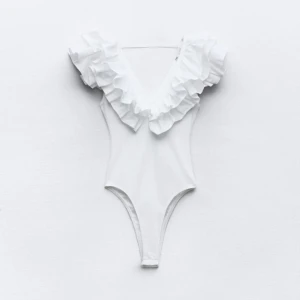 Vit volangbody - Säljer en stilren vit ribbad body med volangdetaljer vid axlarna. Den har en djup v-ringning. Passar bra till både jeans och kjol. Använd 1 gång bara!