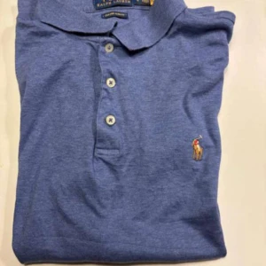 Blå pikétröja från Ralph Lauren - Säljer en klassisk blå pikétröja från Ralph Lauren i storlek L. Tröjan har en broderad logotyp på bröstet och knappar framtill. Perfekt för en stilren look. Gratis frakt ✅🚚