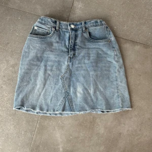 Jeanskjol från Levi Strauss & Co. - Snygg jeanskjol från Levi Strauss & Co. i en klassisk blå denim. Kjolen har en kort längd med rå kant och femficksdesign. Perfekt för en avslappnad stil. Den har en knapp och dragkedja framtill samt en elastisk midja baktill för extra komfort.