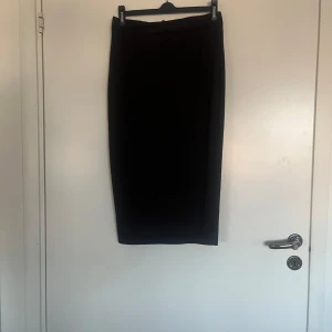 Svart ribbad kjol med slits - Snygg svart ribbad kjol med en stilren slits framtill. Perfekt för en chic look. Kjolen har en tight passform som framhäver figuren.