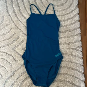 Blå baddräkt från Arena - Snygg blå baddräkt från Arena med smala axelband och enkel design. Perfekt för simträning eller en dag på stranden. Klassisk och stilren look som passar alla tillfällen.