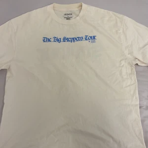 Vit long sleeve från Kendrick Lamar big steppers tour 2022 - Säljer en vit longsleeve från kendrick Lamar’s big steppers tour med tryck 'The Big Steppers Tour '22' på framsidan och 'Not Your Saviour' på baksidan i blått. Tillverkad i 100% bomull, perfekt för en avslappnad stil.