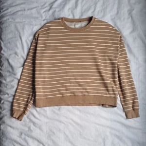 Randig tröja från Pull&Bear - Säljer en snygg beige tröja med vita ränder från Pull&Bear. Tröjan har långa ärmar och en bekväm passform. 