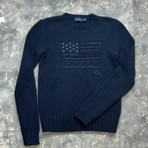 Mörkblå stickad tröja från Polo Ralph Lauren - Säljer en snygg mörkblå stickad tröja från Polo Ralph Lauren. Tröjan har ett coolt stickat mönster av en flagga på framsidan och är i storlek XS. Perfekt för höst och vinter med sin varma och mysiga känsla. Den är i nyskick och redo för nya äventyr!