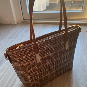 Väska - Säljer denna bruna väska som är helt oanvänd. Köpte för ca 2 år sedan. Har hyfsat bra utrymme med dragkedja. Pris kan diskuteras🩷