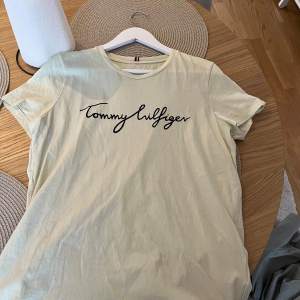 En Ljusgul t-shirt från Tommy Hilfiger. Svart text på framsidan och ett märke på nedre delen av t-shirten. Använd fåtal gånger. Fri från fläckar, märken m.m