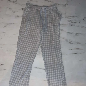 Rutig byxa från Kappahl - Säljer ett par supermysiga och bekväma rutiga byxor från Kappahl i storlek XS. De är i en ljusgrå och vit färgkombination med ett snöre i midjan för justering. Perfekta för en avslappnad dag hemma eller som pyjamasbyxor.