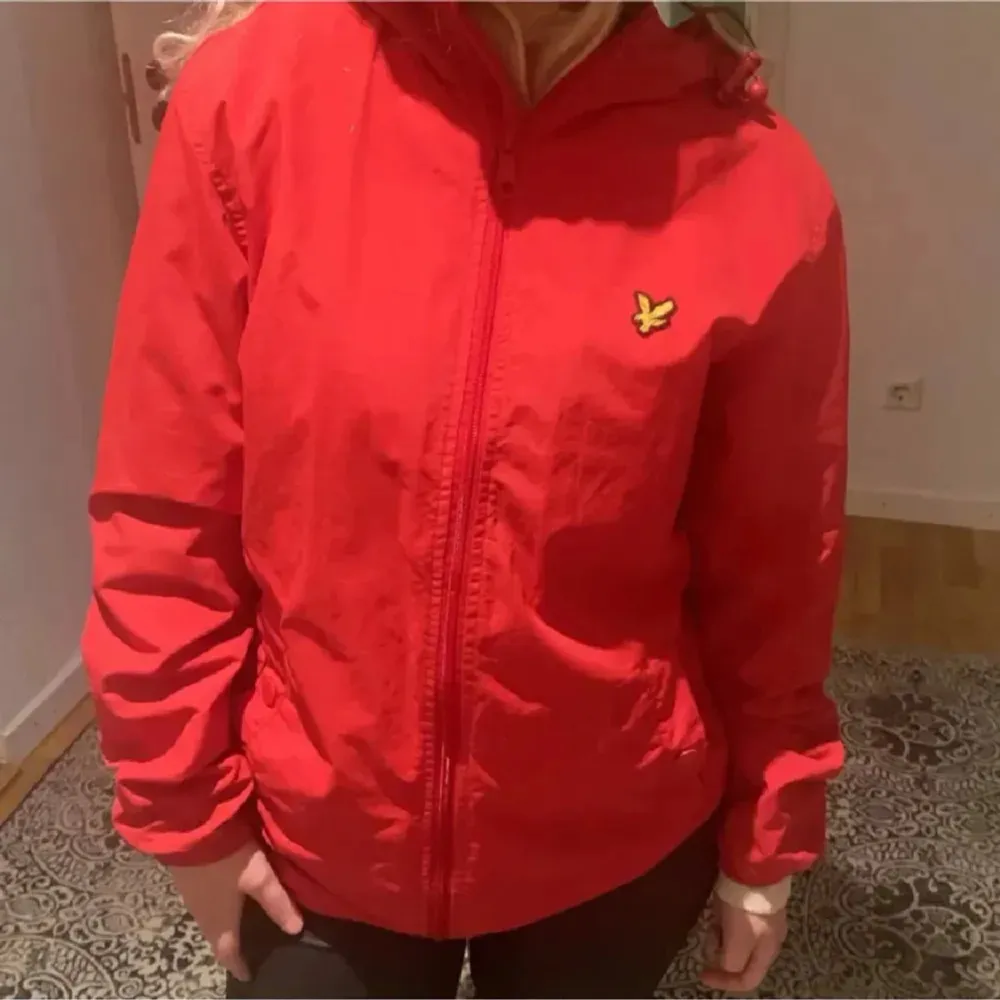 Säljer en snygg röd vindjacka från Lyle & Scott. Jackan har en dragkedja framtill och en huva för extra skydd mot väder och vind. Perfekt för vår och höst!. Jackor.