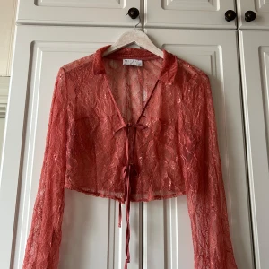 Röd spetsblus från ASOS Design - Säljer en superfin rosa spetsblus från ASOS Design. Den är croppad och har långa ärmar med knytning framtill. spets, fint lite blommigt mönster. ser lite röd ut nå bilden men den är rosa, älskar den men använder aldrig