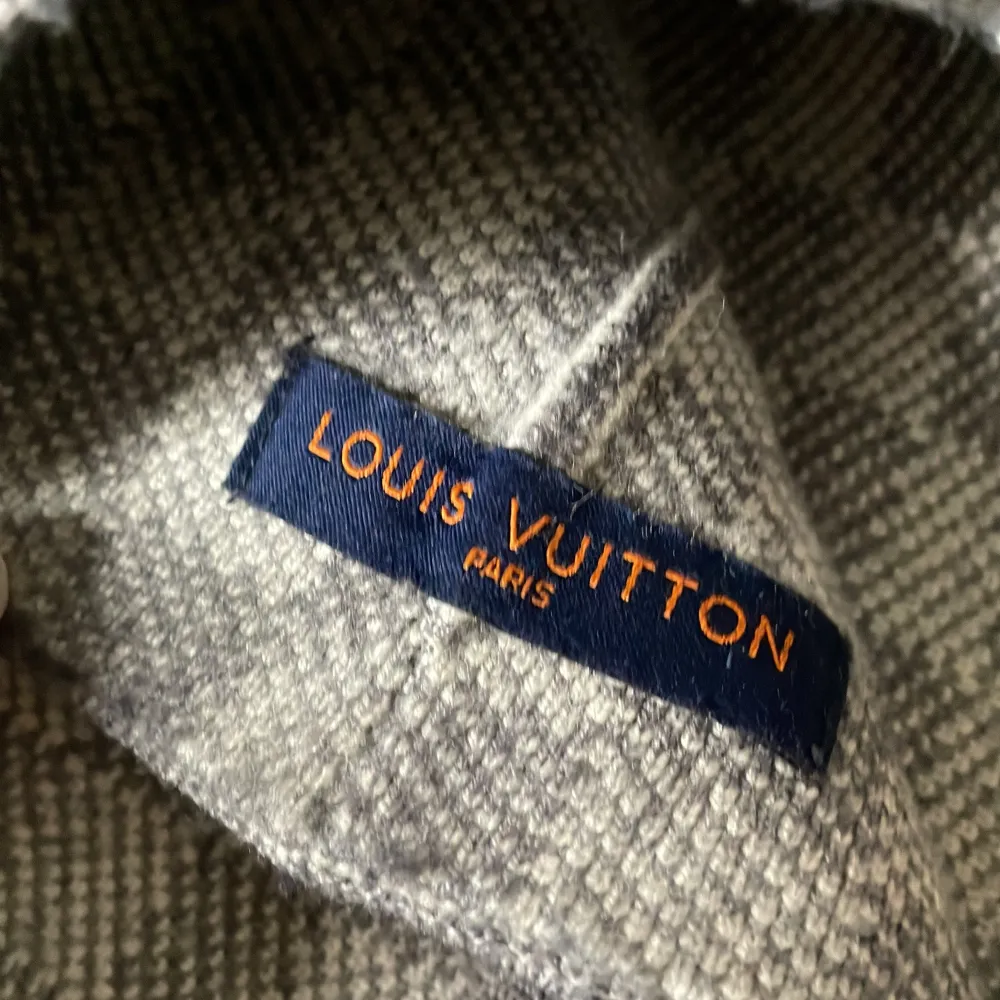 Säljer en stilren och lyxig grå mössa från Louis Vuitton. Den har ett diskret rutigt mönster och är prydd med LV-loggan på uppviket. Perfekt för att hålla sig varm med stil under kyliga dagar.. Accessoarer.