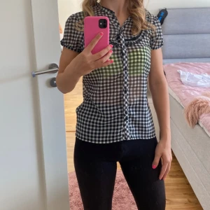 Svartvit rutig blus - Säljer en superfin svartvit rutig blus med korta ärmar. Den har en söt volangdetalj längs knäppningen och en liten spetskant vid halsen. Perfekt för både vardag och fest! 🖤🤍