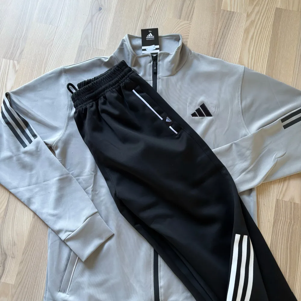 Säljer en snygg grå träningsjacka från Adidas. Jackan har en dragkedja framtill och är långärmad med svarta detaljer på ärmarna. Perfekt för träning eller en avslappnad stil. Den är helt oöppnad. . Sportswear.