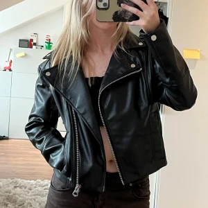 Svart skinnjacka - Säljer en snygg svart skinnjacka med coola detaljer. Jackan är använd ett fåtal gånger då jag har en liknande, så den är i mycket bra skick💕 Från H&M i storlek XS