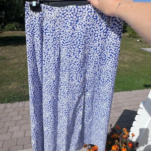 Blommig blå kjol - En blommig blå midikjol med slits längs med vänster ben. Dragkedja bak i ryggen 🌸  Passar mig bra som normalt har mellan storlek S-M i underdelar 🌟  Endast använd en gång!  Längd: 83 cm Midja: 73 cm