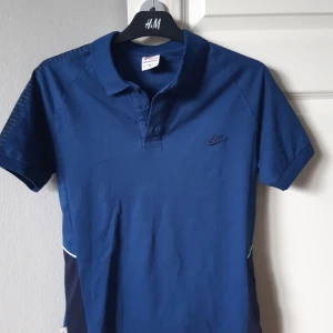 Blå pikétröja från Nike - Säljer en snygg blå pikétröja från Nike i storlek M. Tröjan har korta ärmar och en klassisk krage med knappar. Äldre modell av Nike tränings piké. Fick i present för många år sedan och bara legat i garderoben, vet därför inte vad det är för kvalité. Känns mer som storlek S. Aldrig använd. Perfekt för både vardag och träning. 