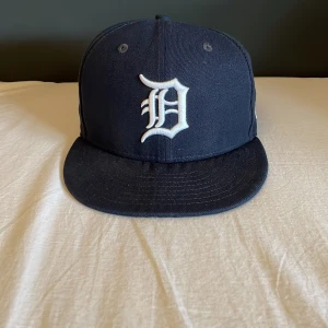 Baseball keps - Det är en basball keps som är använd men i bra skick. Storlek 56,8 och är mörk blå. Laget är Detroit. Skärmen har blivit knäkt men inget som stör.