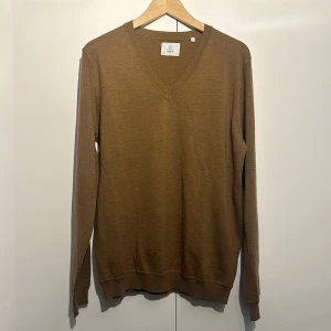 Brun merinoulltröja från Bläck - Säljer en snygg brun tröja i merinoull från Bläck. Den har en stilren v-ringning och är perfekt för både höst och vinter. Tröjan är långärmad och i nyskick, vilket gör den till ett måste i garderoben. Supermjuk och bekväm att ha på sig!