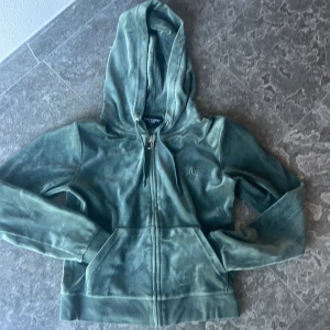 Grön hoodie från Juicy Couture - Säljer en supermjuk och snygg grön hoodie från Juicy Couture. Den har en dragkedja framtill och en praktisk huva. Perfekt för en avslappnad stil eller mysiga dagar hemma. Den är i bra skick och redo för en ny ägare!