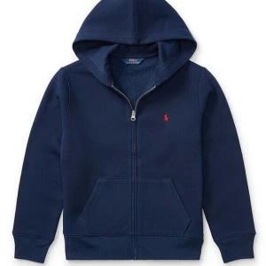 Mörkblå hoodie från Polo Ralph Lauren - Snygg mörkblå hoodie med dragkedja från Polo Ralph Lauren. Den har en klassisk design med en liten röd logotyp på bröstet och en praktisk känguruficka framtill. Perfekt för en avslappnad stil.