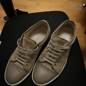Beige sneakers från Lanvin - Snygga beige sneakers från Lanvin i mocka med snörning. Perfekta för en stilren look med en touch av lyx. Skorna har en diskret design med en tålig sula.