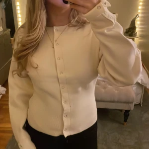 Vit kofta från Gina Tricot - Säljer en stilren vit kofta från Gina Tricot. Den har långa ärmar och knappar framtill samt vid ärmsluten. Perfekt för en elegant och enkel look.