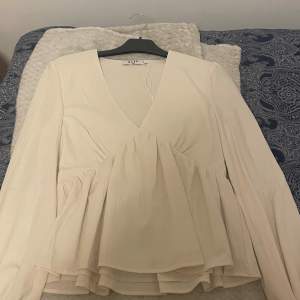 Elegant beige blus från NA-KD med v-ringning och volangdetaljer. Blusen har långa ärmar och en luftig passform, perfekt för en stilren look.