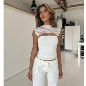 Vit spetsdetaljerad topp - Elegant vit topp med spetsdetaljer över axlar och rygg. Toppen är ärmlös och har en tight passform som framhäver figuren. Helt oanvänd, lappar och plasten kvar🥰 säljer även en likadan röd.