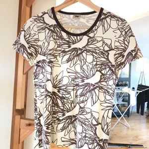 Mönstrad t-shirt från Nanso - Säljer en superfin t-shirt från Nanso i storlek S. Den har ett unikt mönster med fåglar och blommor i brunt och vitt. Perfekt för både vardag och fest! Materialet känns mjukt och skönt mot huden. Passar perfekt till jeans eller kjol.