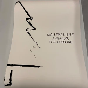 Poster med julcitat - Snygg poster med texten 'Christmas isn't a season, it's a feeling'. Den har en minimalistisk design med en stiliserad julgran i svart på en vit bakgrund. Perfekt för att skapa julstämning i hemmet eller som en fin present till någon som älskar julen. Passar bra i en ram eller direkt på väggen.50x70