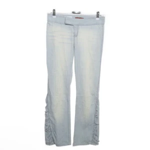 Ljusblå byxor med rynkade detaljer - Snygga ljusblå byxor med unika rynkade detaljer längs benen. Byxorna har en bootcut-stil och en låg midja som ger en smickrande passform. Perfekta för en trendig look💕 midjemåttet tvärs över är 38 cm, innnerbenslämgden är 75cm, 19 cm grenhöjd och hela längden är 89cm💕