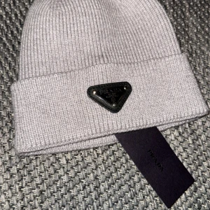 Grå ribbad mössa från Prada - Snygg grå ribbad mössa från Prada med ett stilrent metallmärke framtill. Perfekt för att hålla värmen med stil under kyliga dagar.