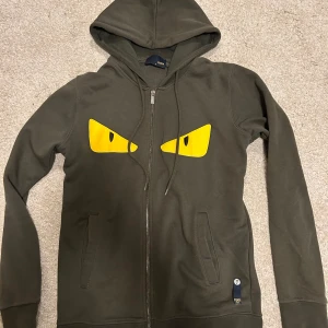 Fendi kofta - Säljer en mörk grön kofta från Fendi med gula ögon på framsidan. Tröjan har dragkedja och är i mycket bra skick. Perfekt för höst och vår, med långa ärmar och en skön passform. Passar både storlek S och M