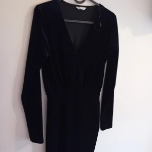 Svart sammet klänning - Snygg svart klänning i sammet med långärmad design och v-ringning. Perfekt för en elegant kväll eller fest. Klänningen har en tight passform som framhäver figuren.