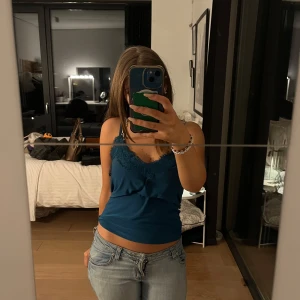 Blå linne med spetsdetaljer - Säljer ett snyggt blått linne med spetsdetaljer vid halsringningen. Perfekt för sommardagar eller en utekväll. Linnet är i bra skick och har en bekväm passform. Passar perfekt till jeans eller kjol!