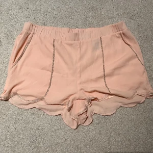 Rosa shorts från H&M - Säljer ett par söta rosa shorts från H&M i storlek M. De har en pärldetalj längs kanten och en dragkedja bak. Materialet känns mjukt och bekvämt.