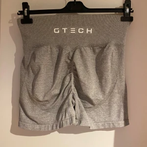 Grå shorts från GTech - Säljer ett par grå shorts från GTech i storlek L. De är tillverkade av 90% nylon och 10% spandex, vilket gör dem superstretchiga och bekväma. Perfekta för träning eller gym.  De har en hög midja och en tight passform som ger bra stöd. Shortsen har en scrunch samt konturer som framhäver rumpan supersnyggt. Nypris 399kr.