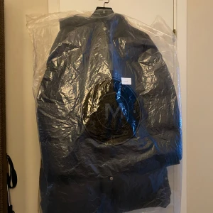 Svart dunjacka från Monel - Säljer en svart dunjacka från Monel med lång ärm och dragkedja. Jackan är perfekt för kalla vinterdagar och har en stilren design med en hög krage och knappar framtill. Nypris 6500:- 