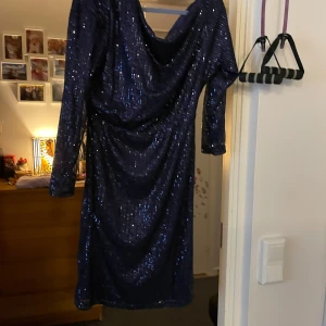 Mörkblå glittrig klänning - Snygg mörkblå klänning med glittriga paljetter och draperad design. Klänningen har långa ärmar och en elegant passform som passar perfekt för festliga tillfällen.helt ny