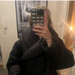 Svart pufferjacka - Säljer en supermysig svart pufferjacka som är perfekt för kalla dagar. Passformen är lite oversized och den stora kragen är sååå varm och gosig. Jackan är i mycket bra skick, lappen är kvar och den passar perfekt för både höst och vinter. Den är långärmad och har en stilren design utan onödiga detaljer. Säljer för jag köpte en annan!💝