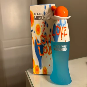 Moschino Cheap and Chic I Love Love Parfym - En färgglad och lekfull parfymflaska från Moschino med en unik design. Flaskan är blå med en orange och vit topp, och kommer i en matchande förpackning med livliga mönster. Doften är fräsch och ungdomlig, perfekt för den som älskar att lukta fräscht.